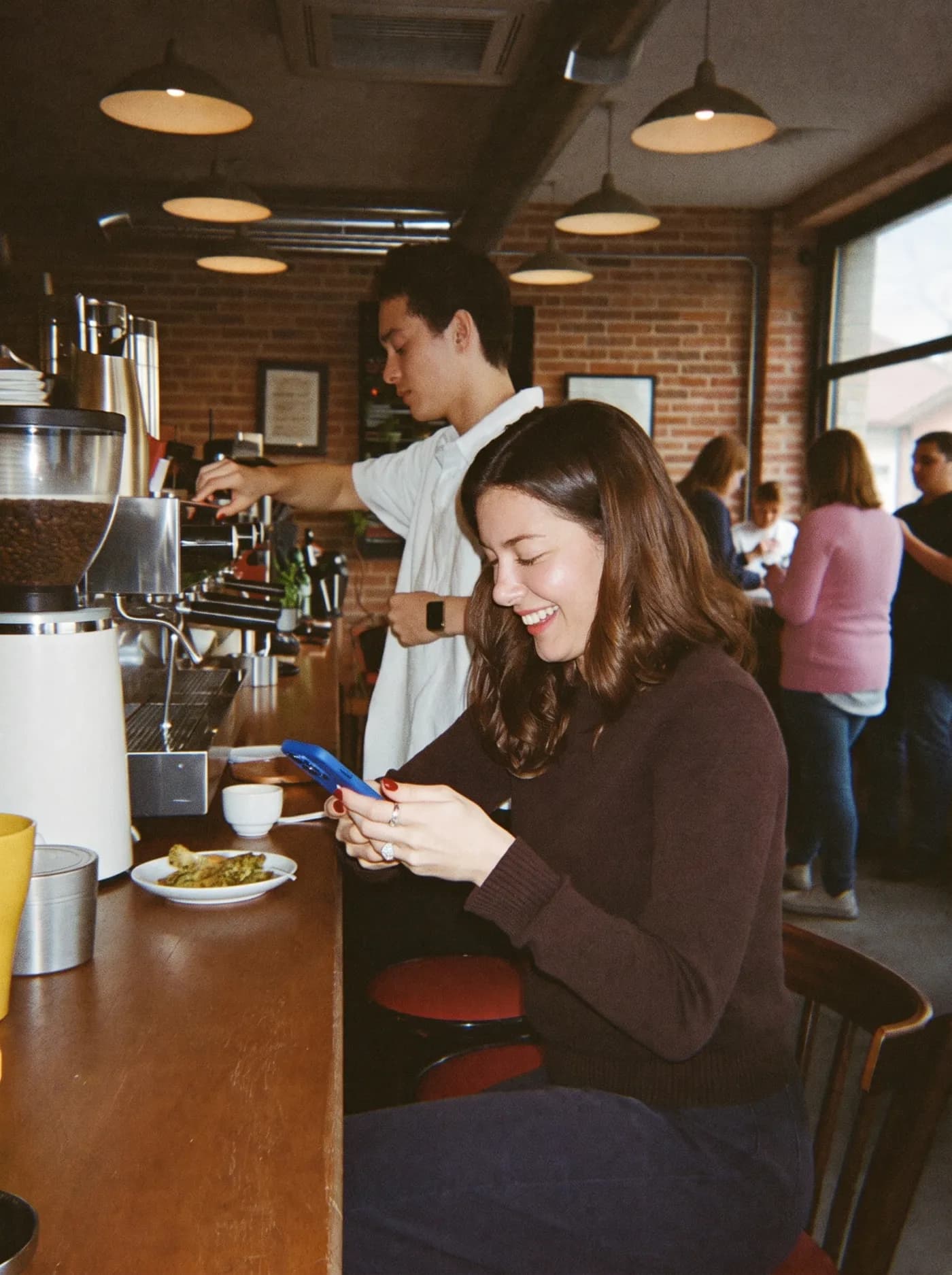 A smiling customer typing on her phone at a coffee shop counter